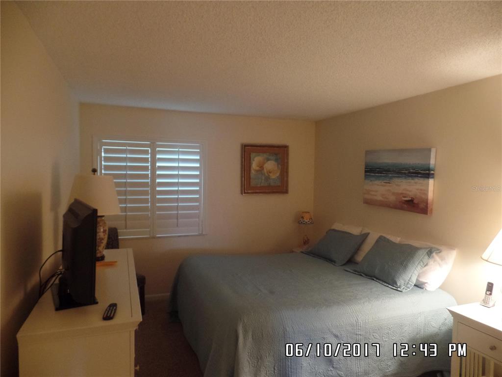 A bedroom features a bed with blue bedding, a white dresser with a television, and shutters — 815 OCEAN SHORE BOULEVARD UNIT 9, ORMOND BEACH, FL