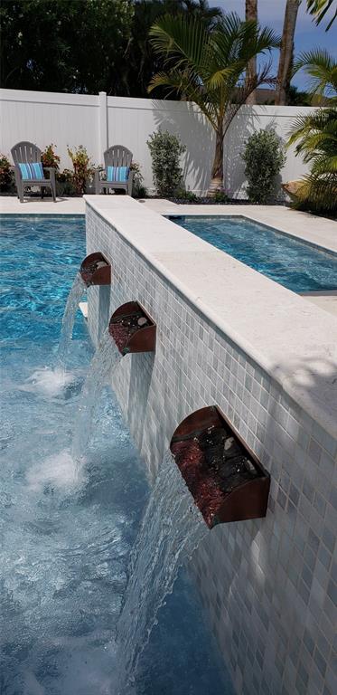 A swimming pool features a tiled wall with three copper water scuppers pouring into the water — 430 173RD AVENUE E, NORTH REDINGTON BEACH, FL