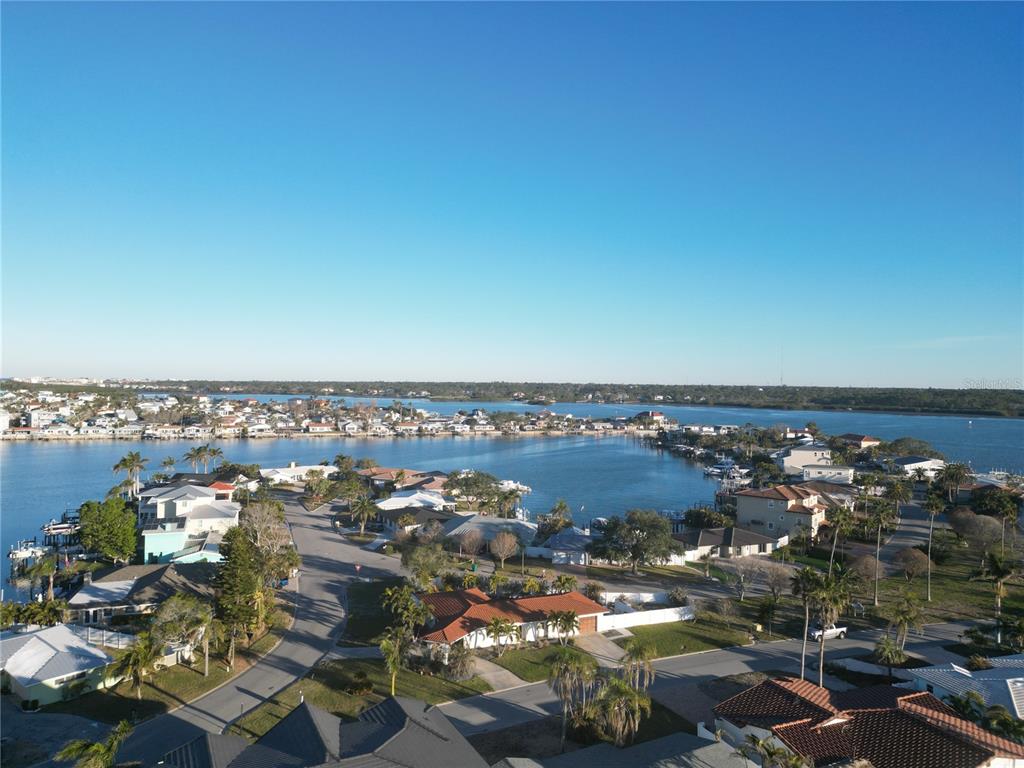 An aerial view shows waterfront houses along a bay with palm trees and clear skies — 430 173RD AVENUE E, NORTH REDINGTON BEACH, FL
