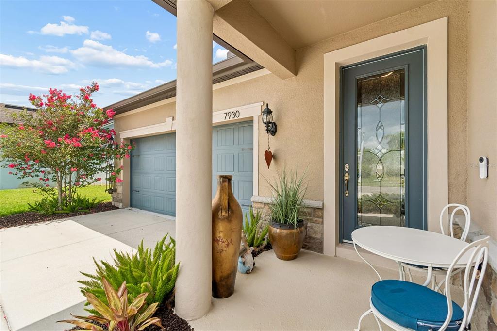 A covered front porch features a blue door, a white bistro set, and potted plants — 7930 OLIVE BROOK DRIVE, WESLEY CHAPEL, FL