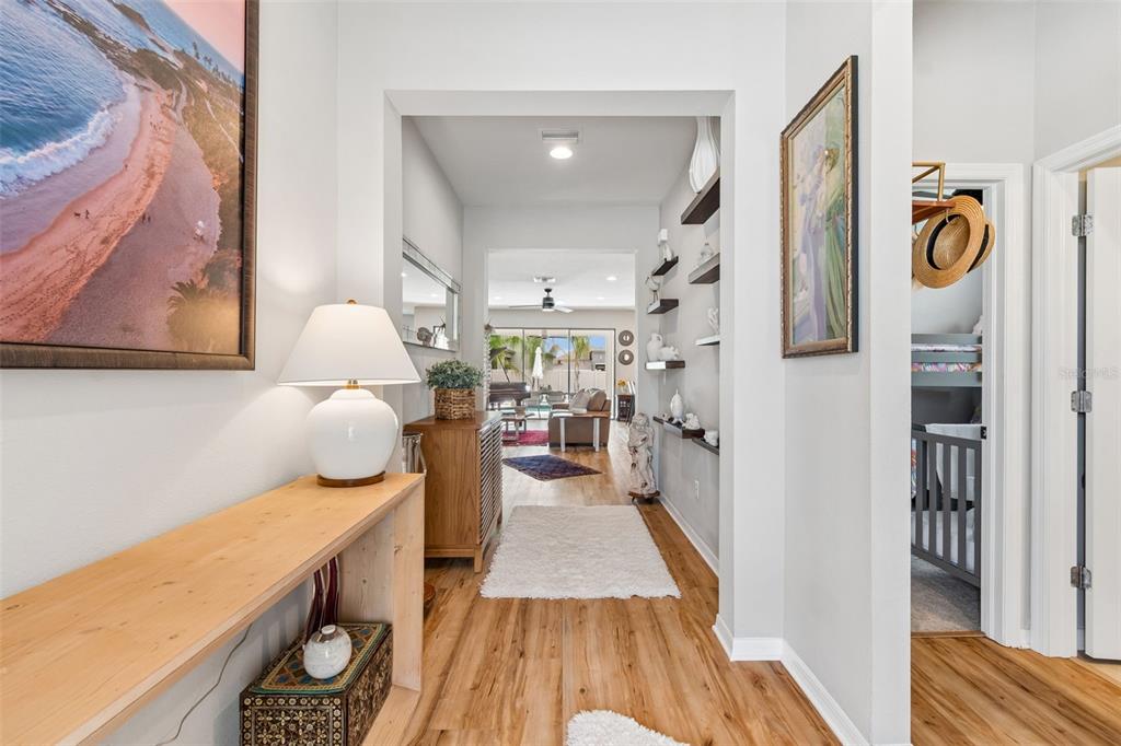 A bright hallway features wood-look flooring, a console table with a lamp, and wall shelving — 7930 OLIVE BROOK DRIVE, WESLEY CHAPEL, FL