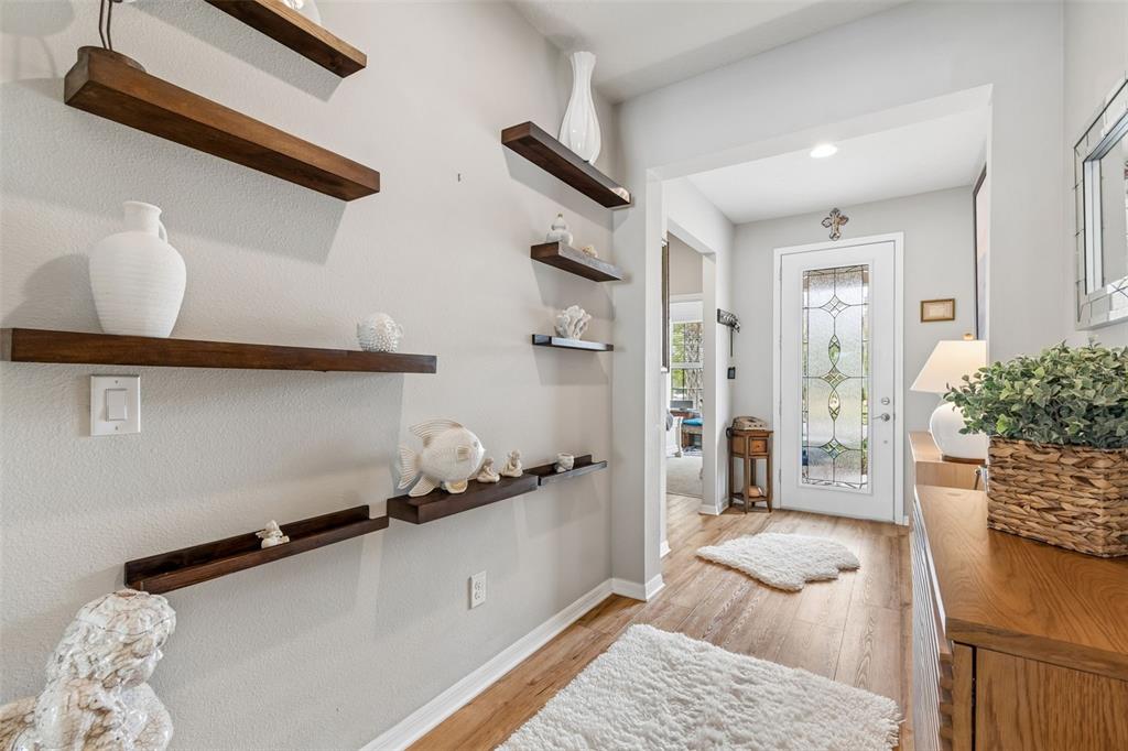 A bright entryway features wood-toned floating shelves, light walls, wood flooring, and a glass-paneled door — 7930 OLIVE BROOK DRIVE, WESLEY CHAPEL, FL