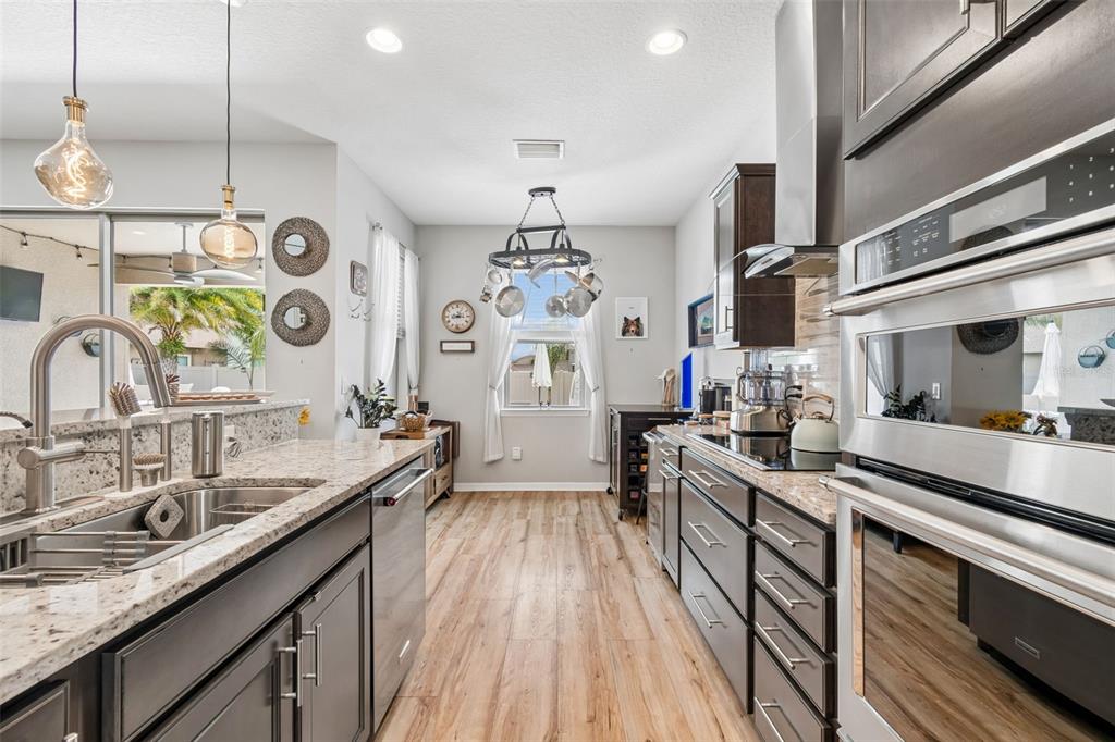 A modern kitchen features dark cabinets, granite countertops, stainless steel appliances, and a hanging pot rack — 7930 OLIVE BROOK DRIVE, WESLEY CHAPEL, FL