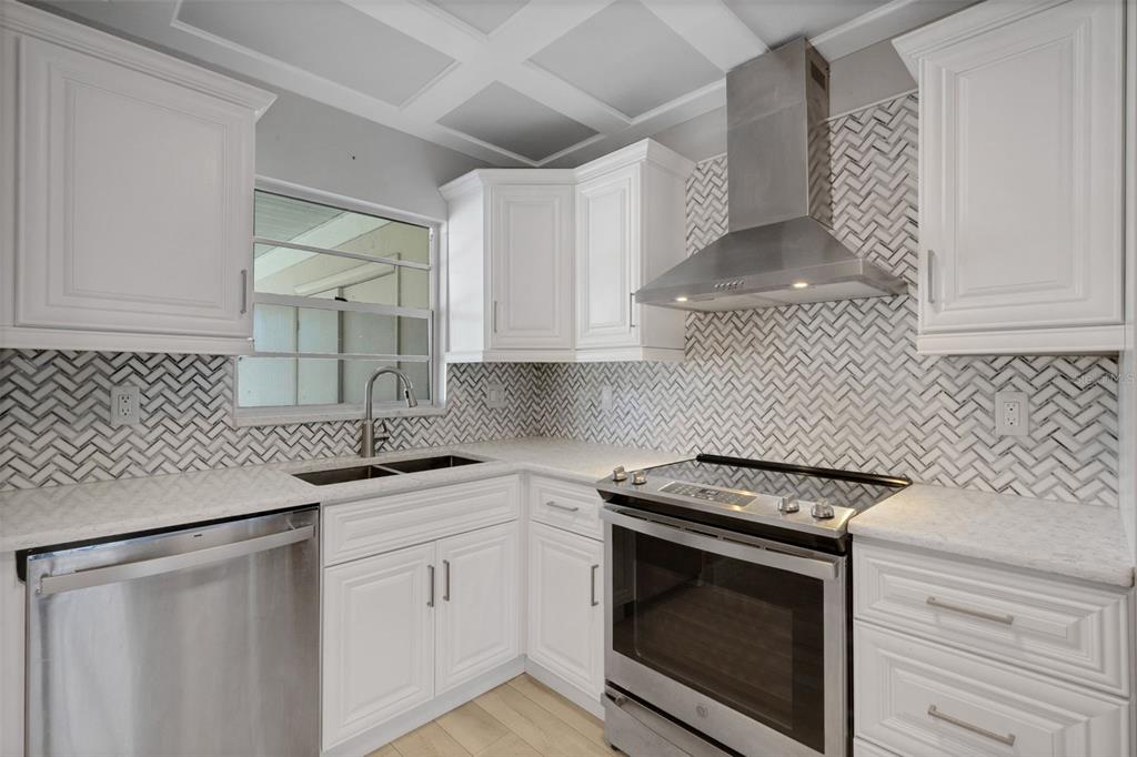 A modern kitchen features white cabinetry, stainless steel appliances, light wood flooring, and a coffered ceiling — 4602 PARK ACRES DRIVE UNIT 96, BRADENTON, FL