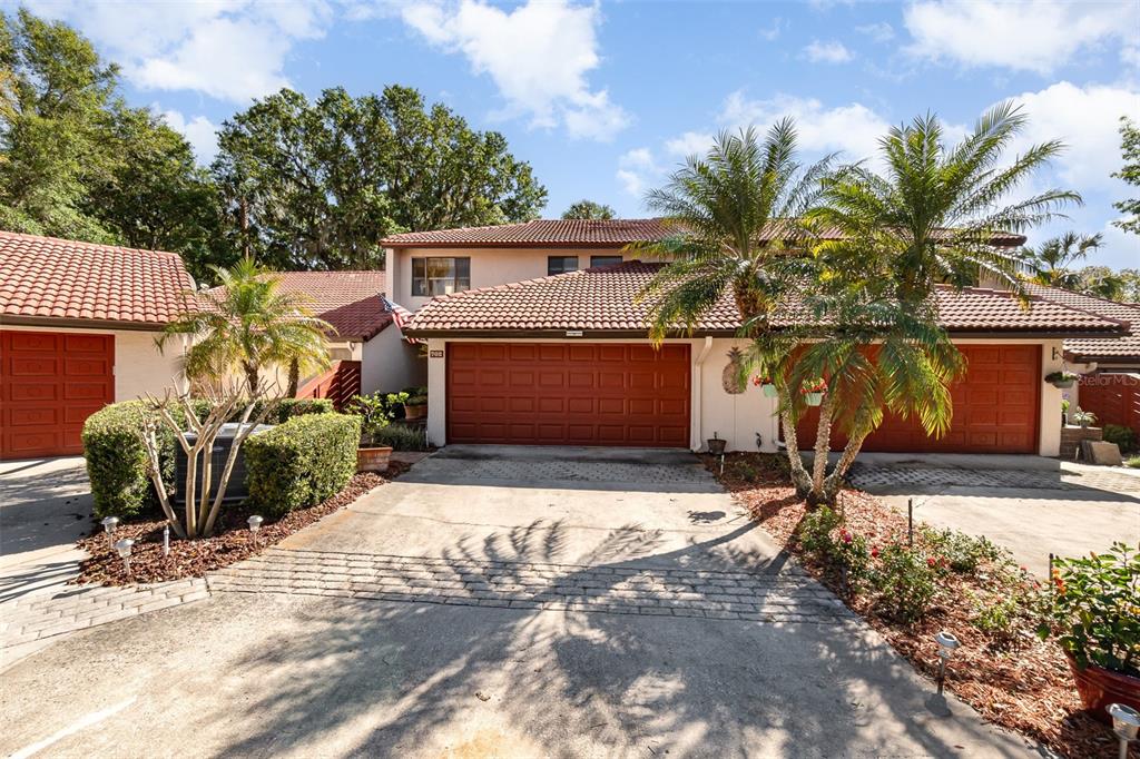 A two-story townhouse exterior features two red garage doors, a concrete driveway, and palm trees — 702 CLUSTERWOOD DRIVE, YALAHA, FL
