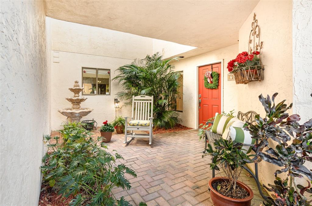 A brick-paved patio features a fountain, a rocking chair, a bench, and a red door — 702 CLUSTERWOOD DRIVE, YALAHA, FL