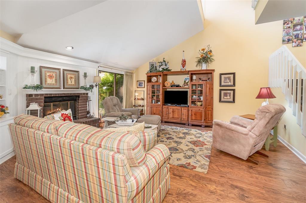 A living room with a brick fireplace, plaid sofa, wooden entertainment center, and vaulted ceiling — 702 CLUSTERWOOD DRIVE, YALAHA, FL