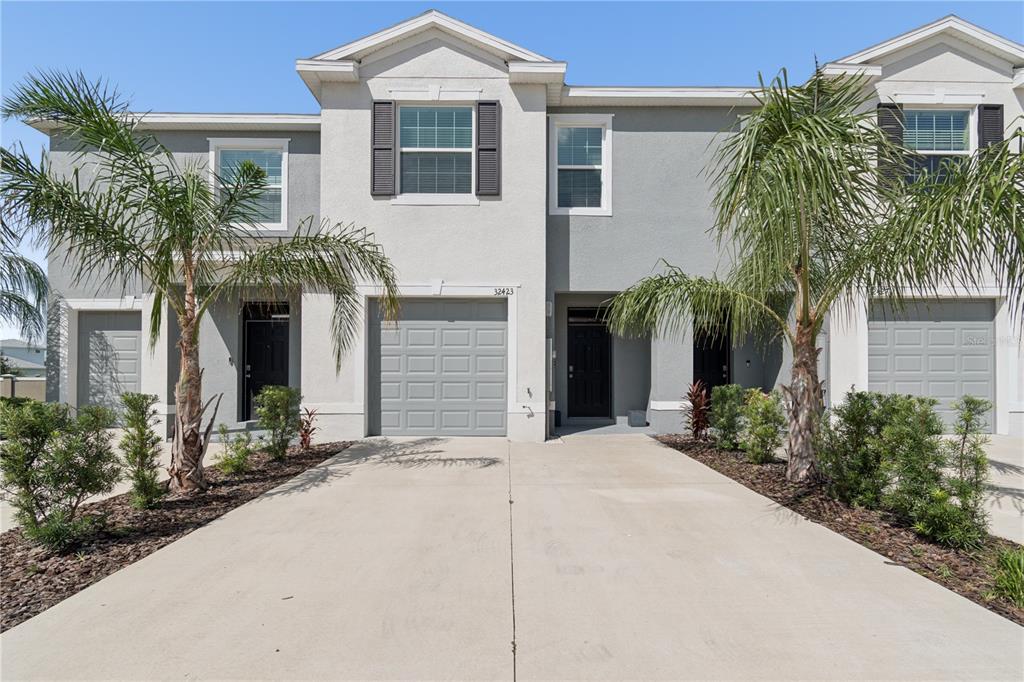 A two-story townhouse exterior features gray stucco walls, a concrete driveway, and two palm trees — 32423 TURTLE GRACE LOOP, WESLEY CHAPEL, FL