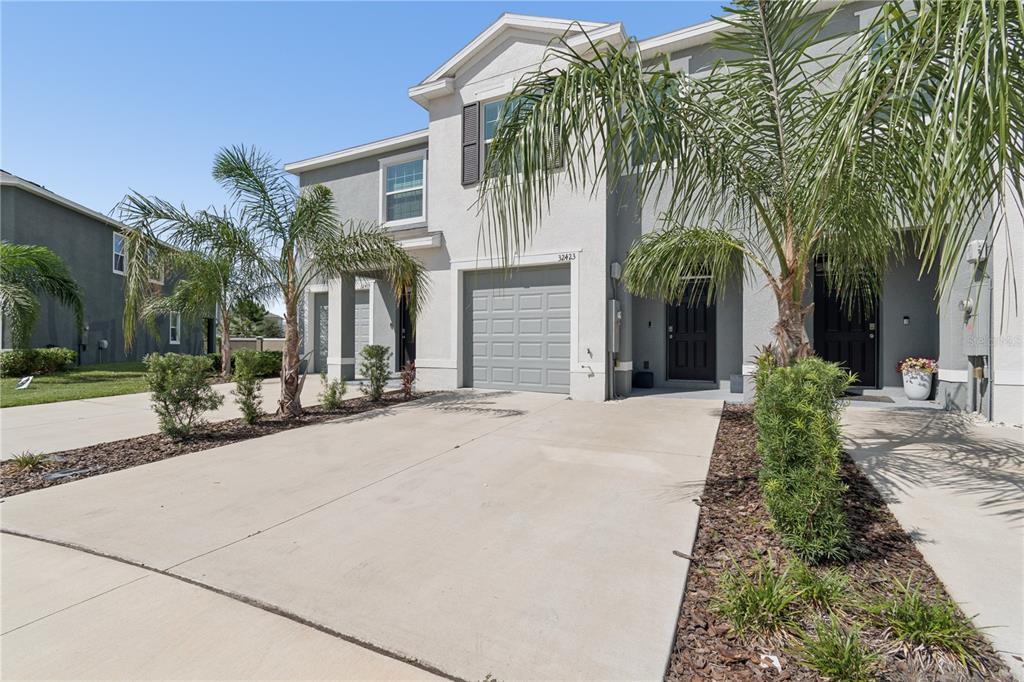 A two-story townhouse with a gray exterior, a single-car garage, and palm trees in front — 32423 TURTLE GRACE LOOP, WESLEY CHAPEL, FL
