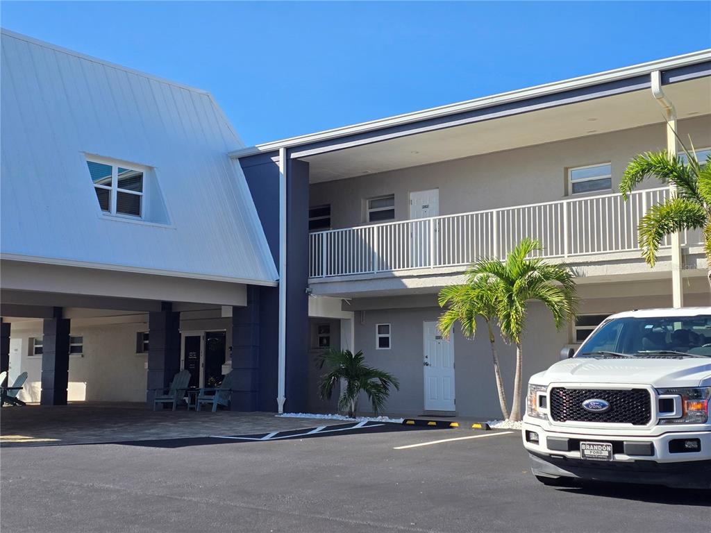 A two-story building with a white metal roof, a balcony, and a parked white truck — 3453 GULF OF MEXICO DRIVE UNIT 242, LONGBOAT KEY, FL