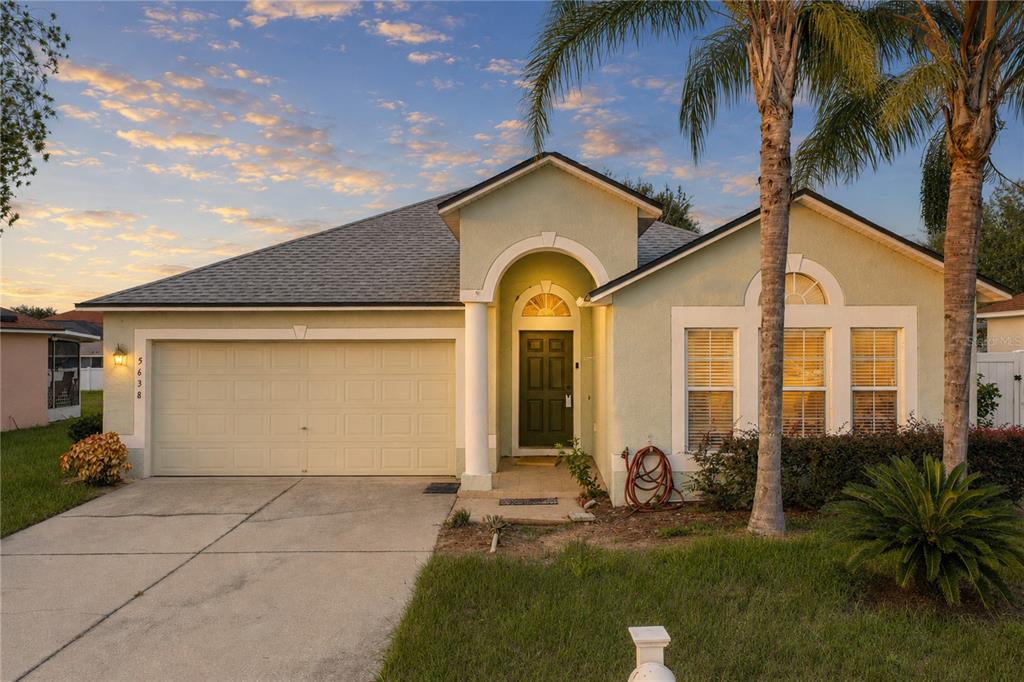 A single-story house with a light green stucco exterior, a two-car garage, and palm trees — 5638 ROYAL HILLS STREET, WINTER HAVEN, FL