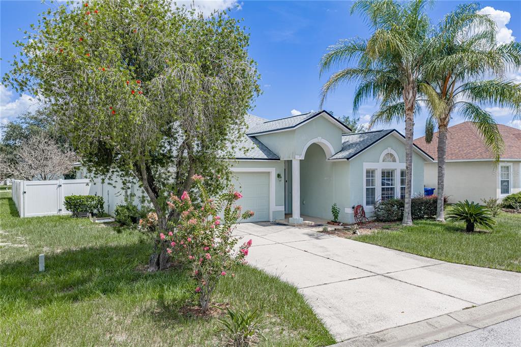A light green single-story house with a concrete driveway, a palm tree, and a white fence — 5638 ROYAL HILLS STREET, WINTER HAVEN, FL
