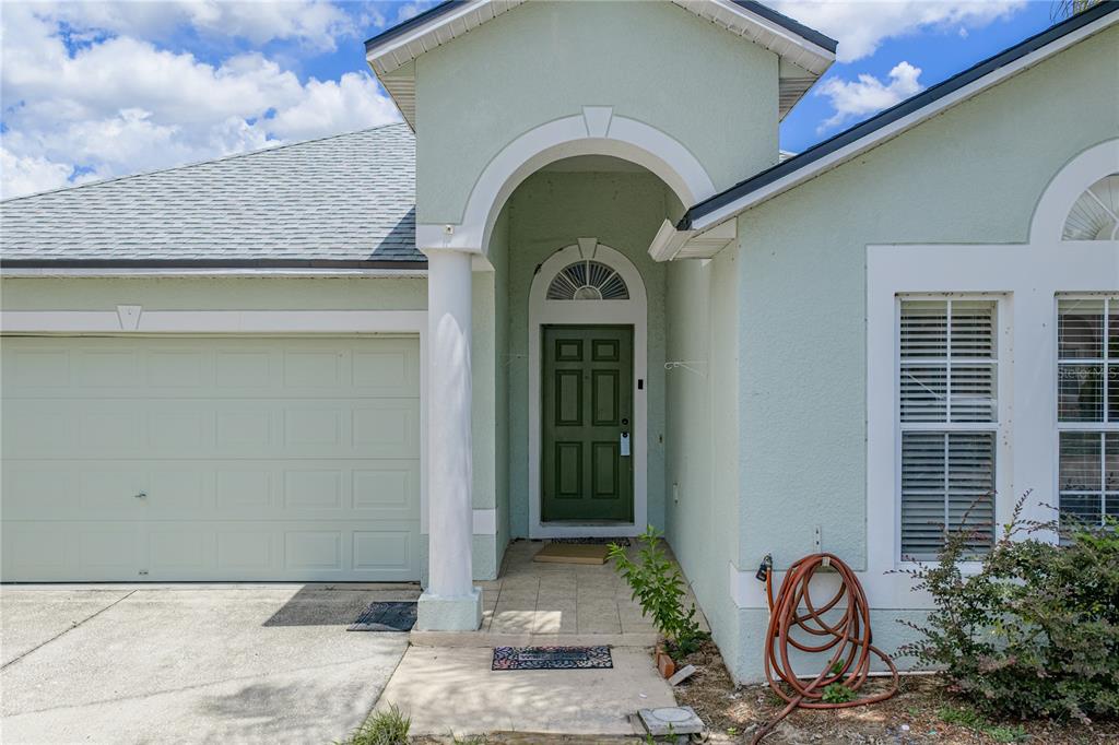 The exterior of a light green house features a garage, a covered entryway, and a door — 5638 ROYAL HILLS STREET, WINTER HAVEN, FL