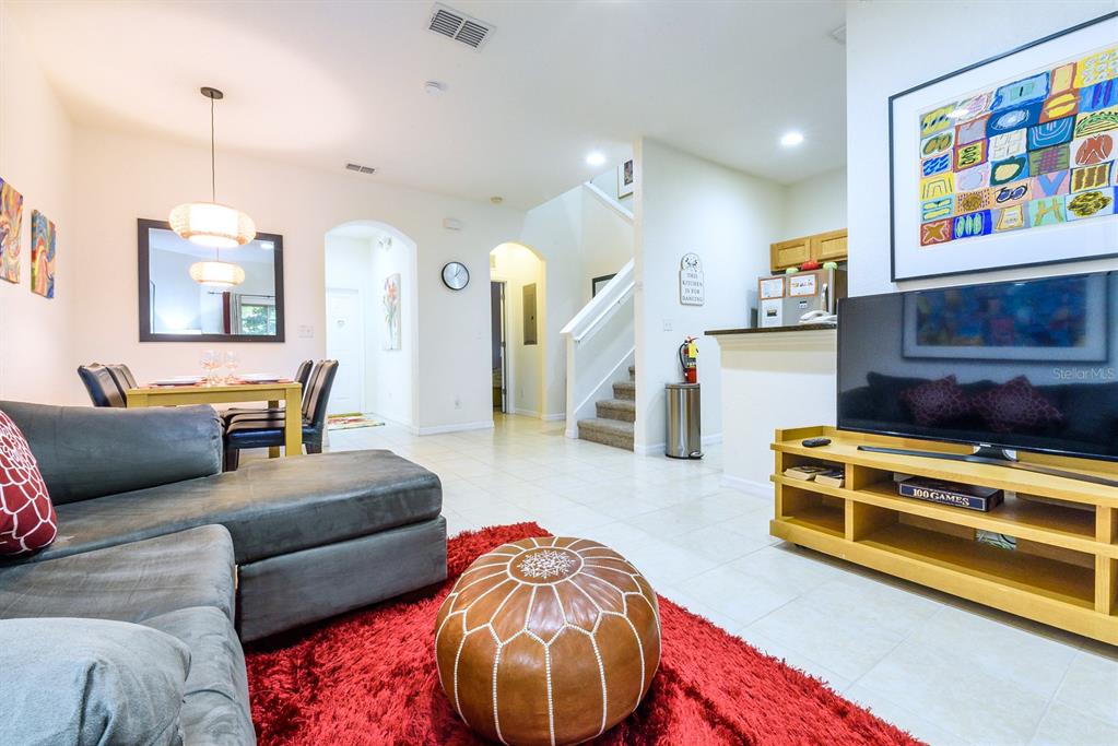 A living room with a grey sectional, red rug, leather ottoman, and an adjacent dining area — 2725 COUPE STREET, KISSIMMEE, FL