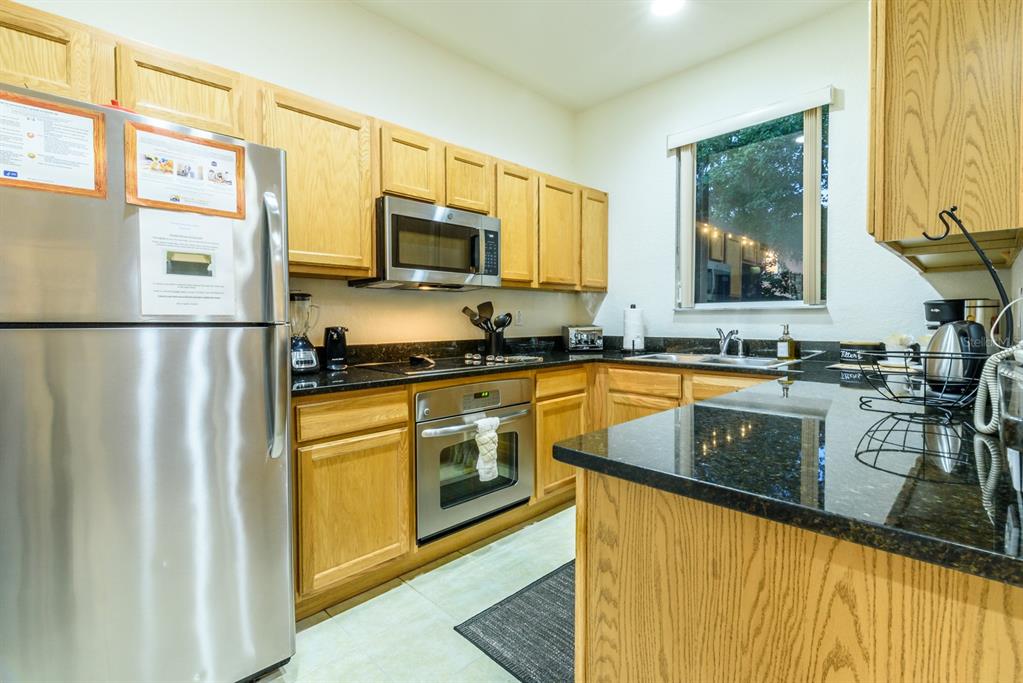 A kitchen features light oak cabinets, black granite countertops, and stainless steel appliances — 2725 COUPE STREET, KISSIMMEE, FL