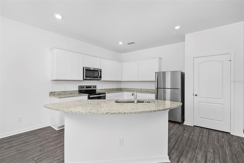 A kitchen with white cabinets, granite countertops, stainless steel appliances, and wood-look flooring — 572 BAY LEAF DRIVE, POINCIANA, FL