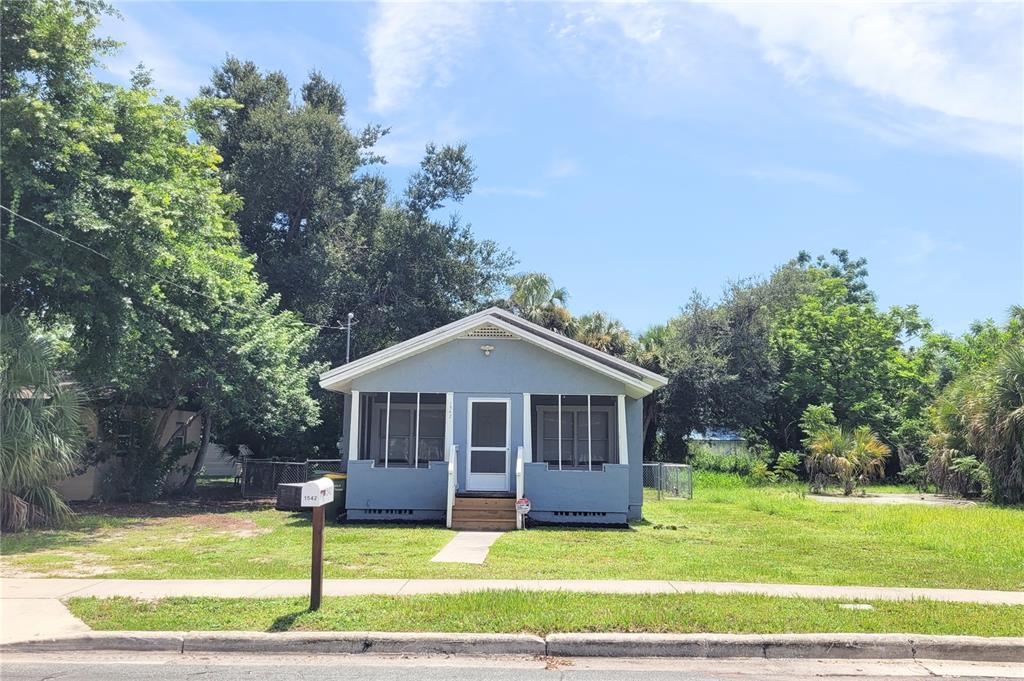 A small, light blue, single-story house with a screened front porch sits on a grassy lot — 1542 29TH STREET, SARASOTA, FL