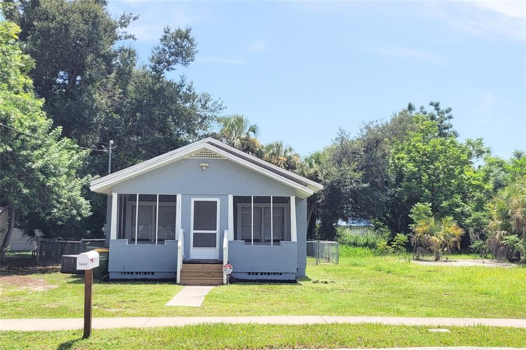 A small, light blue, single-story house with a screened-in front porch and a grassy yard — 1542 29TH STREET, SARASOTA, FL