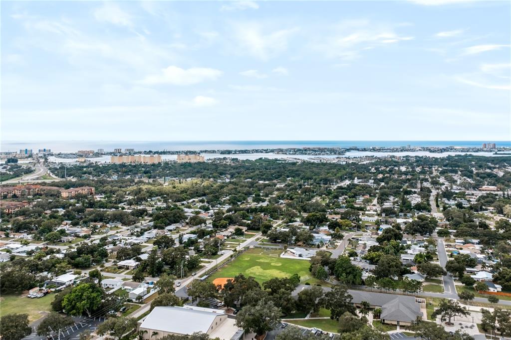 An aerial view shows a suburban neighborhood with a park, trees, and distant coastal water — 9976 56TH AVENUE N, ST PETERSBURG, FL
