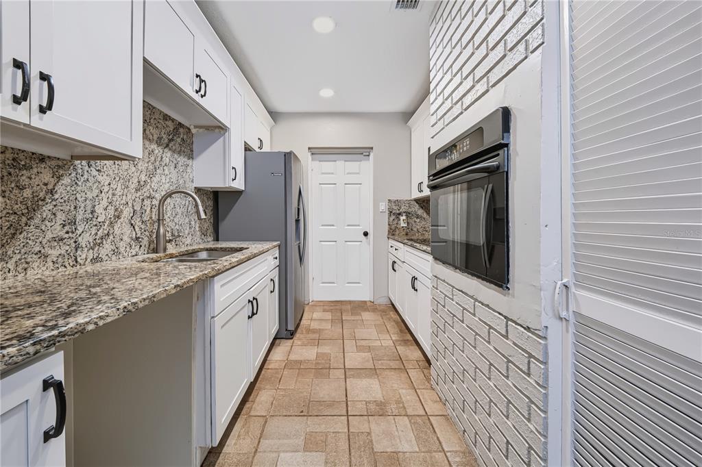 A galley kitchen features white cabinets, granite countertops, a brick-encased wall oven, and tile flooring — 9976 56TH AVENUE N, ST PETERSBURG, FL