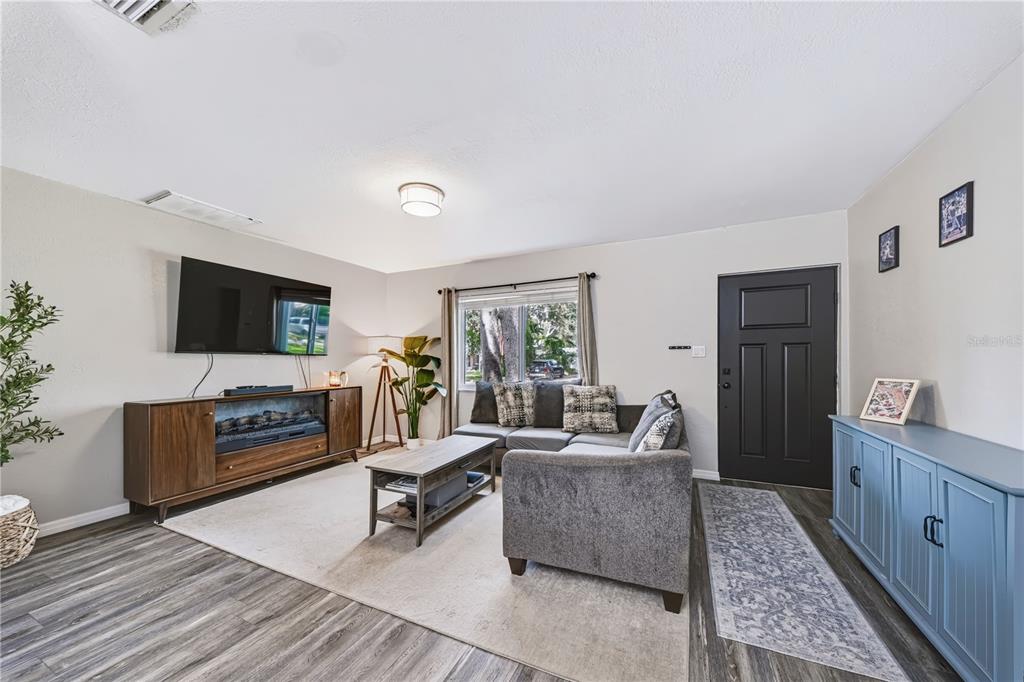 A living room features a grey sectional sofa, a television, and a blue storage cabinet — 9976 56TH AVENUE N, ST PETERSBURG, FL