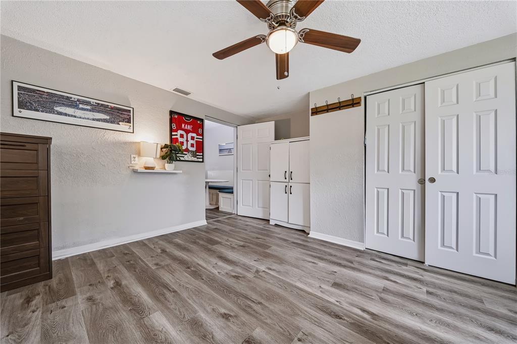 A bedroom with light gray walls, wood-look flooring, a ceiling fan, and white closet doors — 9976 56TH AVENUE N, ST PETERSBURG, FL
