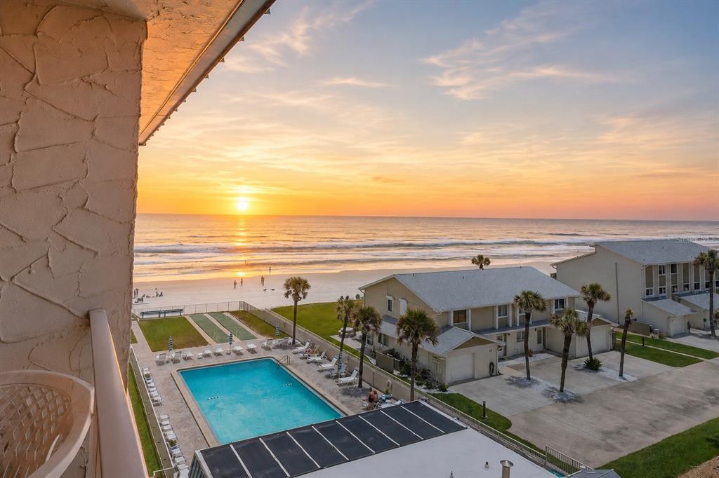 An elevated view of a beachside swimming pool and buildings at sunset — 4201 S ATLANTIC AVENUE UNIT 503, NEW SMYRNA BEACH, FL