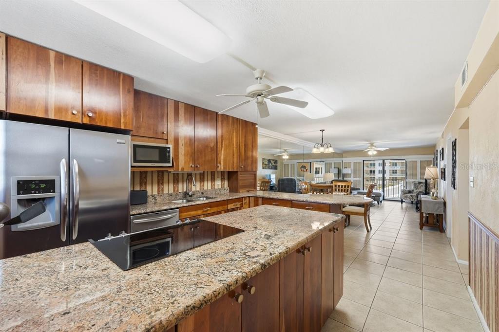 A kitchen with wood cabinets, granite countertops, and a stainless steel refrigerator opens to living — 4201 S ATLANTIC AVENUE UNIT 503, NEW SMYRNA BEACH, FL