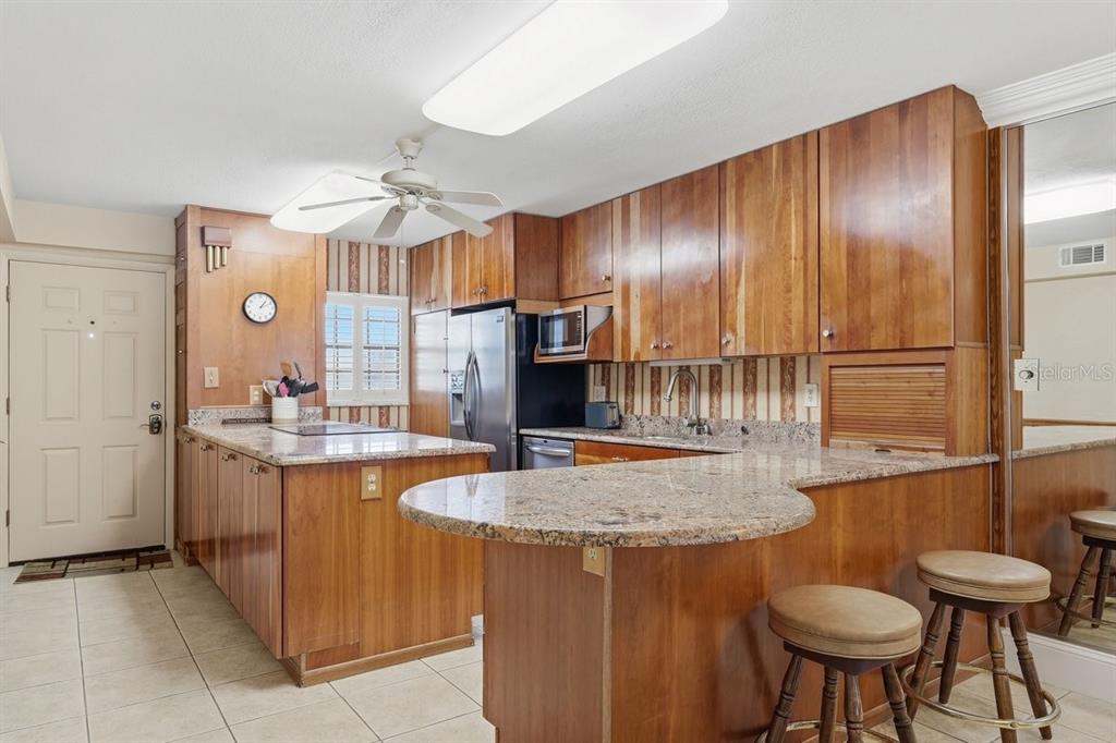 A kitchen features wood cabinetry, granite countertops, a breakfast bar, and a ceiling fan — 4201 S ATLANTIC AVENUE UNIT 503, NEW SMYRNA BEACH, FL