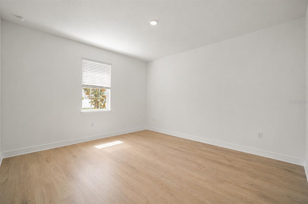 An empty bedroom features white walls, light wood-look flooring, and a single window with blinds — 1304 SILO DRIVE, ST CLOUD, FL