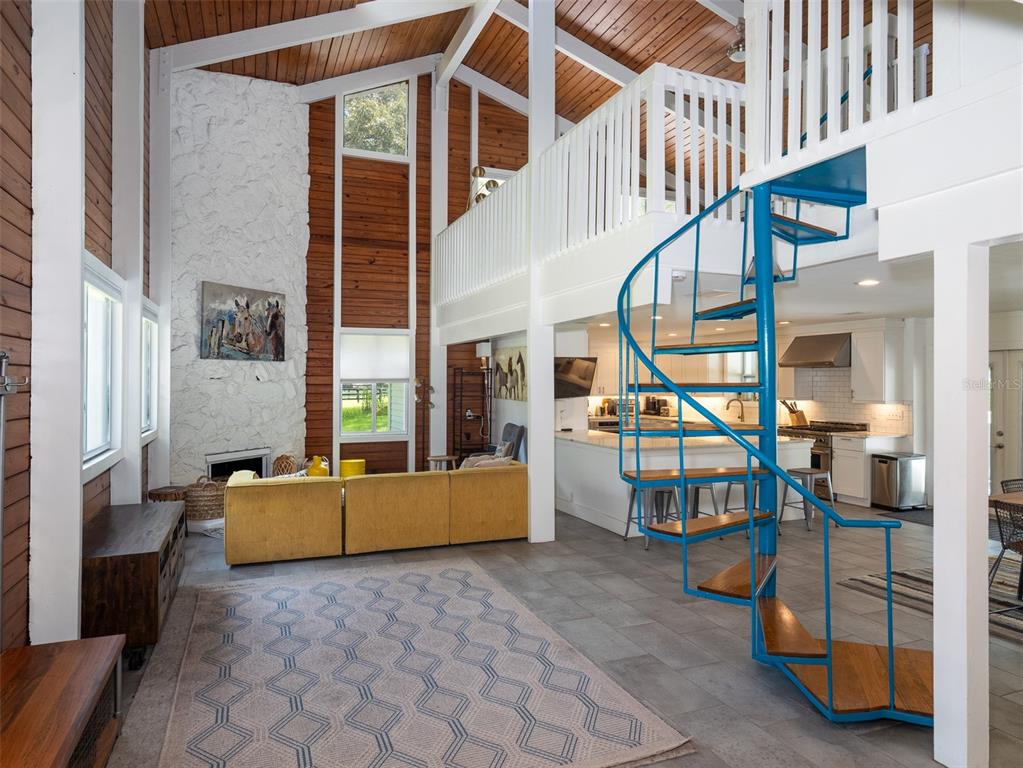 A living room with a stone fireplace, wood walls, and a blue spiral staircase — 9255 NW 115TH AVENUE, OCALA, FL