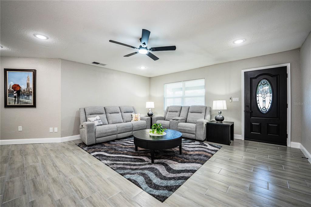 A living room features gray tile flooring, a patterned area rug, and two gray sofas — 2250 MAPLE HILL DRIVE, LAKELAND, FL