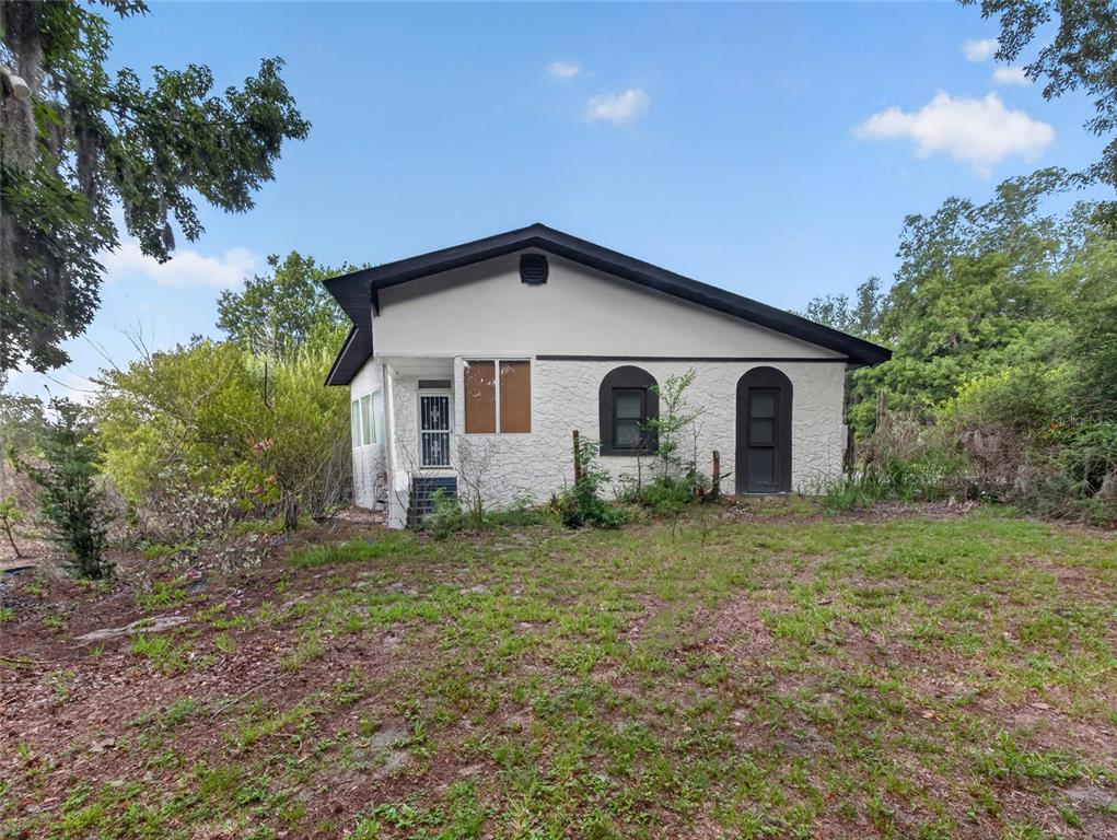 A white stucco house with a dark roof and arched doorways sits on a grassy lot — 14820 COUNTY ROAD 48, ASTATULA, FL