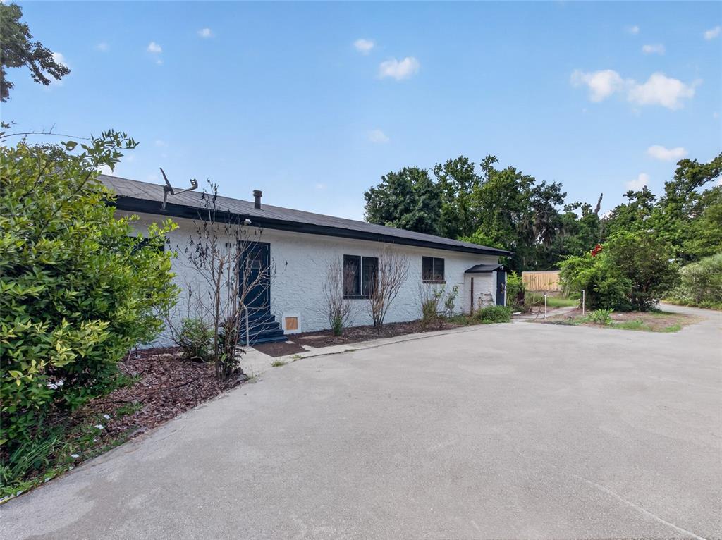 A single-story white stucco building with a dark roof sits beside a large concrete driveway — 14820 COUNTY ROAD 48, ASTATULA, FL