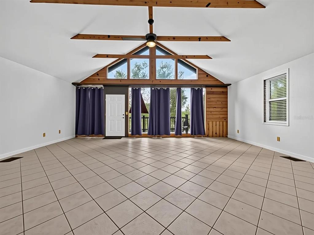 A spacious room features vaulted ceilings with exposed beams, tile flooring, and large windows — 14820 COUNTY ROAD 48, ASTATULA, FL