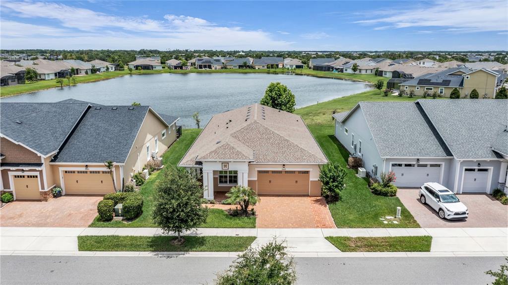 An aerial view shows three suburban houses with garages and driveways facing a large pond — 2665 MEADOWEDGE LOOP, ST CLOUD, FL