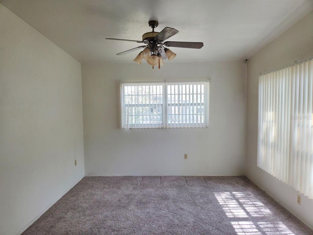 An empty room features beige carpet, white walls, a ceiling fan, and vertical window blinds — 640 FORREST DR, BARTOW, FL
