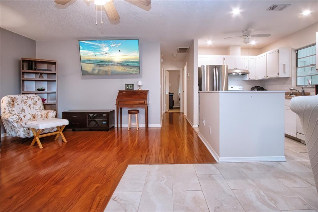 A living room with wood flooring features a floral armchair, a television, and an open kitchen — 2228 GREENHAVEN DRIVE UNIT 384, SUN CITY CENTER, FL