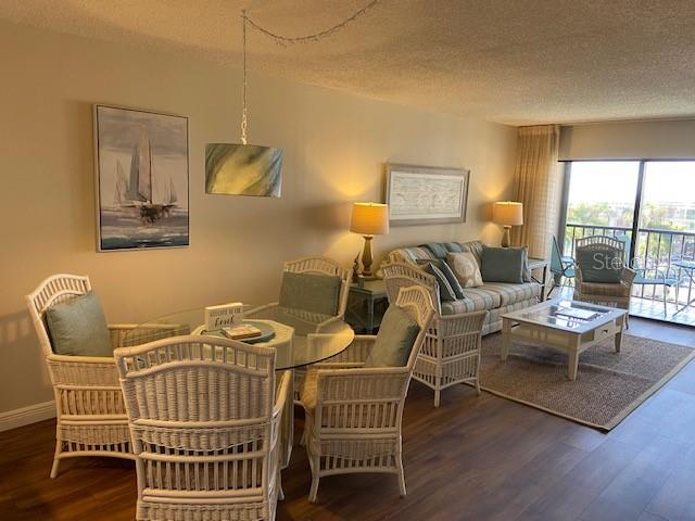 A living and dining area features wicker furniture, a glass table, and a balcony view — 1001 BENJAMIN FRANKLIN DRIVE UNIT 507, SARASOTA, FL