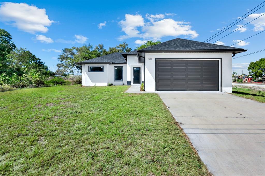 A single-story white house with a dark roof and garage sits on a grassy lot — 100 PARISH DRIVE, LEHIGH ACRES, FL
