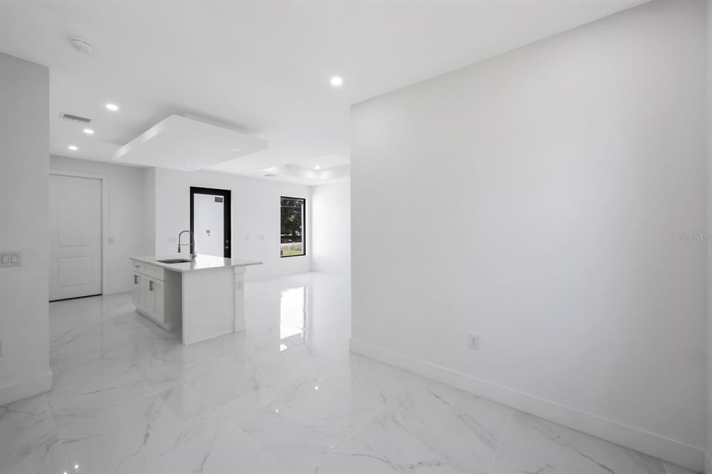 A bright, modern kitchen and living area feature white marble floors and white cabinetry — 100 PARISH DRIVE, LEHIGH ACRES, FL