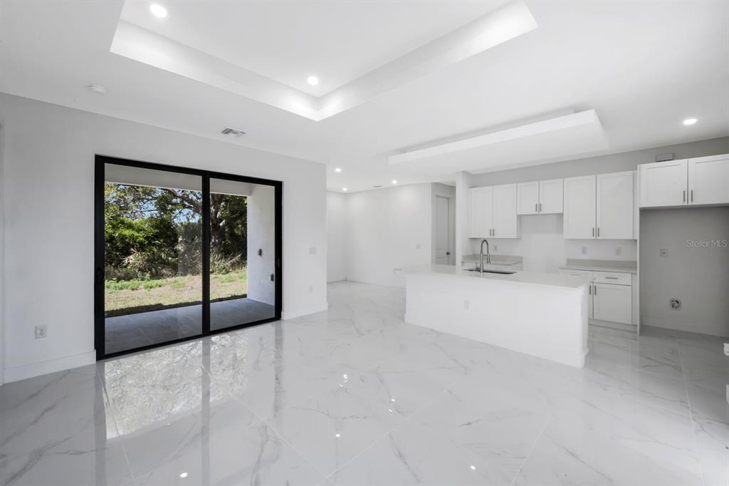 A modern kitchen and living area with white cabinets, marble-style tile floors, and sliding doors — 100 PARISH DRIVE, LEHIGH ACRES, FL
