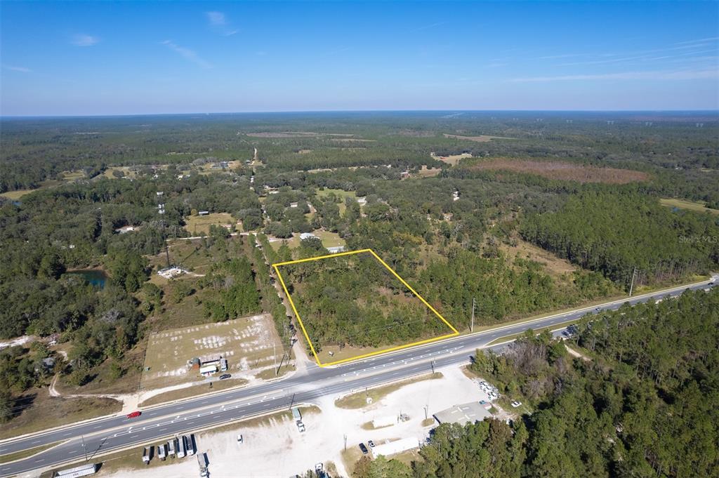 An aerial view shows a rectangular plot of land outlined in yellow along a highway — 108 WILLIS ROAD, INTERLACHEN, FL