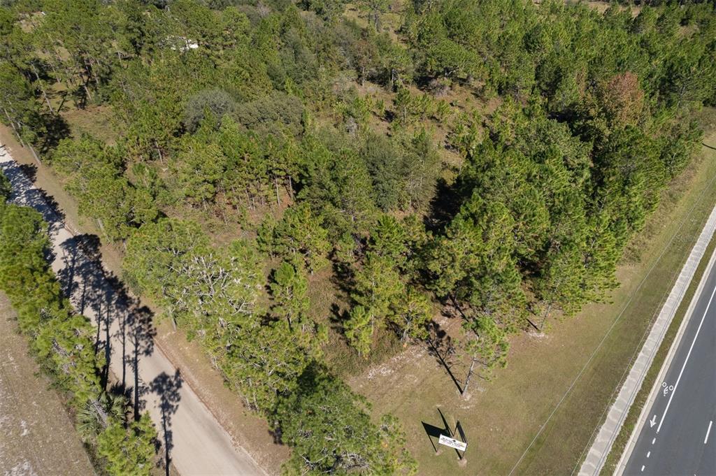 An aerial view shows a wooded, undeveloped plot of land situated between a road and highway — 108 WILLIS ROAD, INTERLACHEN, FL