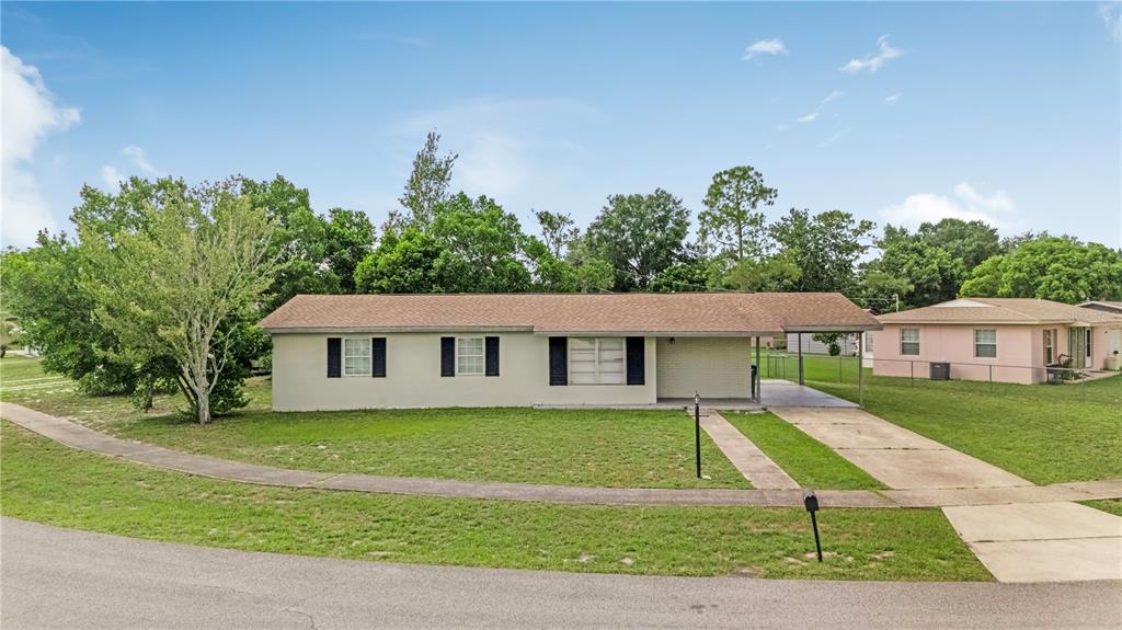 A single-story house with a carport, light-colored exterior, and dark shutters sits on a lawn — 962 ROCKHILL STREET, DELTONA, FL