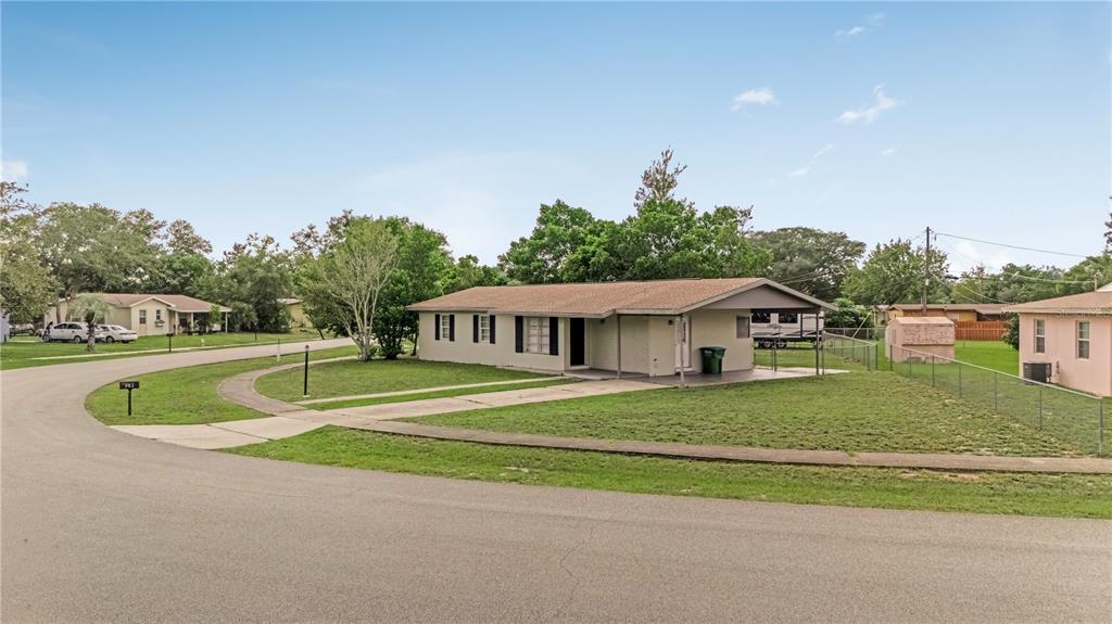 A single-story house with a tan exterior and a covered porch sits on a corner lot — 962 ROCKHILL STREET, DELTONA, FL