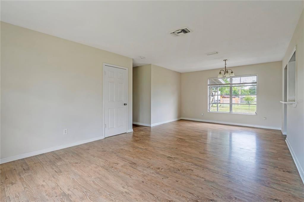 An empty room with light wood-look flooring, beige walls, a white door, and a window — 962 ROCKHILL STREET, DELTONA, FL