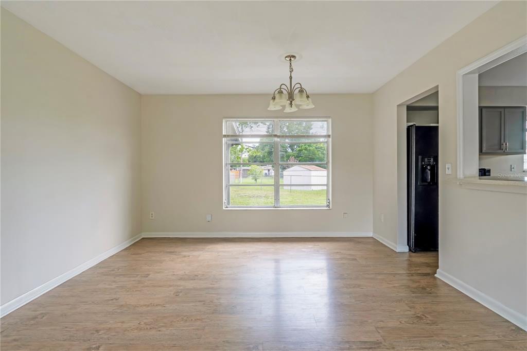 An empty dining room features light wood-look flooring, beige walls, a central chandelier, and a window — 962 ROCKHILL STREET, DELTONA, FL