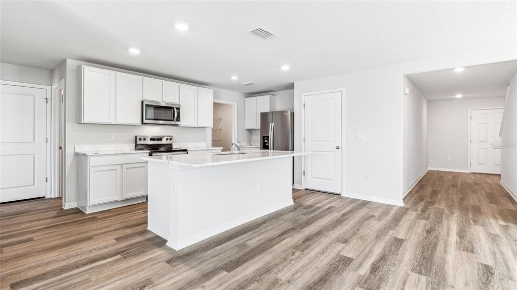A kitchen with white cabinets, stainless steel appliances, a marble-topped island, and wood-look flooring — 1729 COBB TRAIL, PARRISH, FL