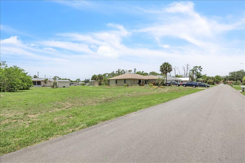 A paved road runs alongside a large, grassy vacant lot with houses in the background — 1274 CORAL LANE, ENGLEWOOD, FL